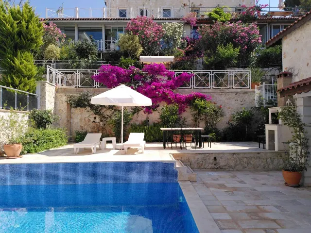 BookNoFees vacation rental in Kalkan, Kas, Antalya, Antalya, Turkey – Pool terrace with sun loungers, umbrella, and flowering bougainvillea on stone walls