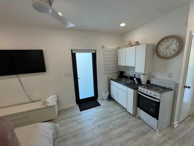 BookNoFees vacation rental in Cutler Bay, United States – Studio kitchen with white cabinets, gas stove, wall clock, and glass door