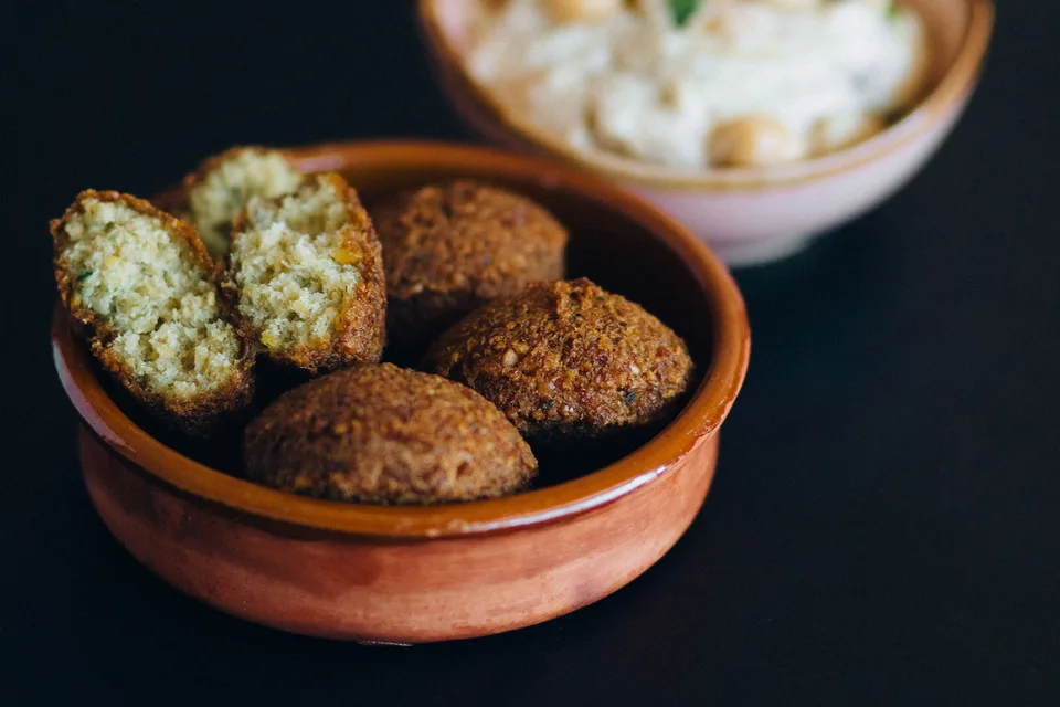 BookNoFees: Halimbawa ng larawan: Mga bola ng falafel, kabilang ang isang hiwang bukas, sa isang mangkok na may hummus sa likuran