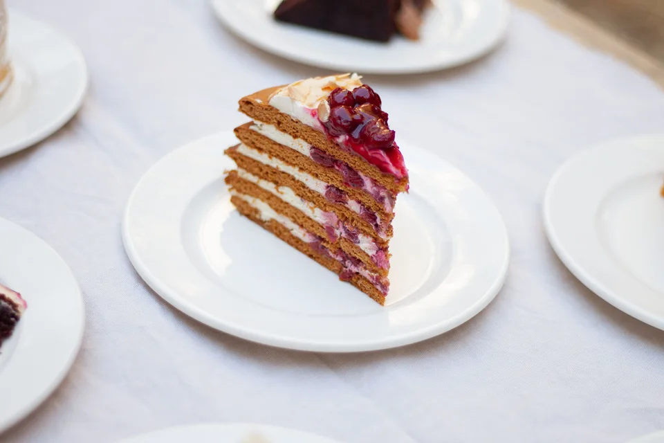 BookNoFees: Halimbawa ng larawan: Isang hiwa ng layered cake na may mga berry sa ibabaw sa isang puting plato