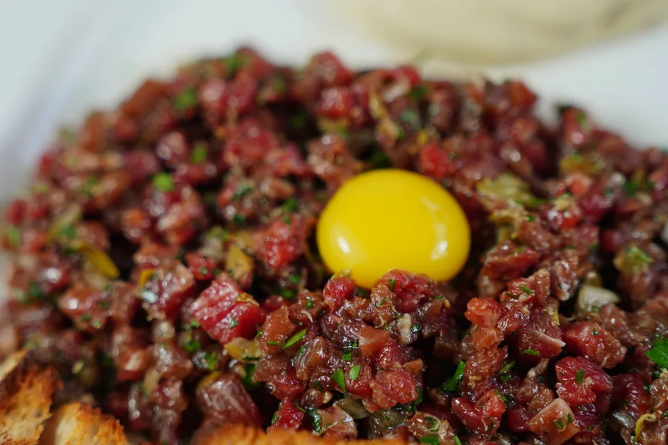 BookNoFees: Halimbawa ng larawan: Steak tartare na may itlog na pula sa ibabaw at inihain kasama ang tinustang tinapay